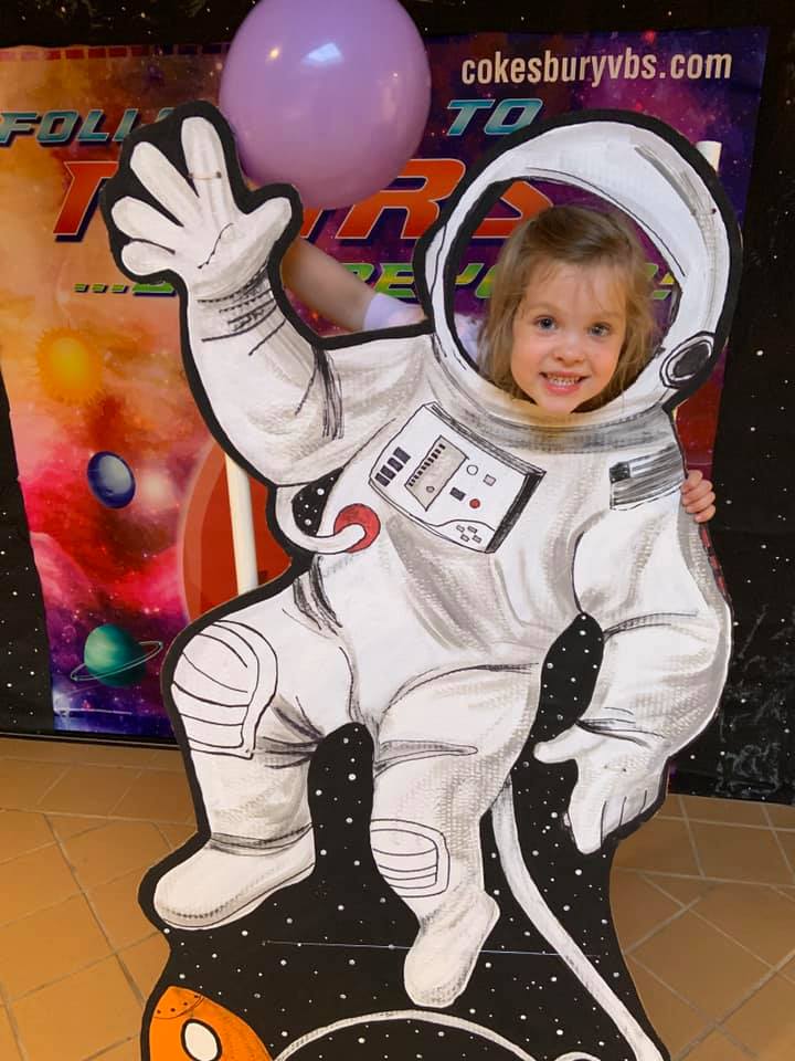 Young girl sticks her head through an astronaut cutout
