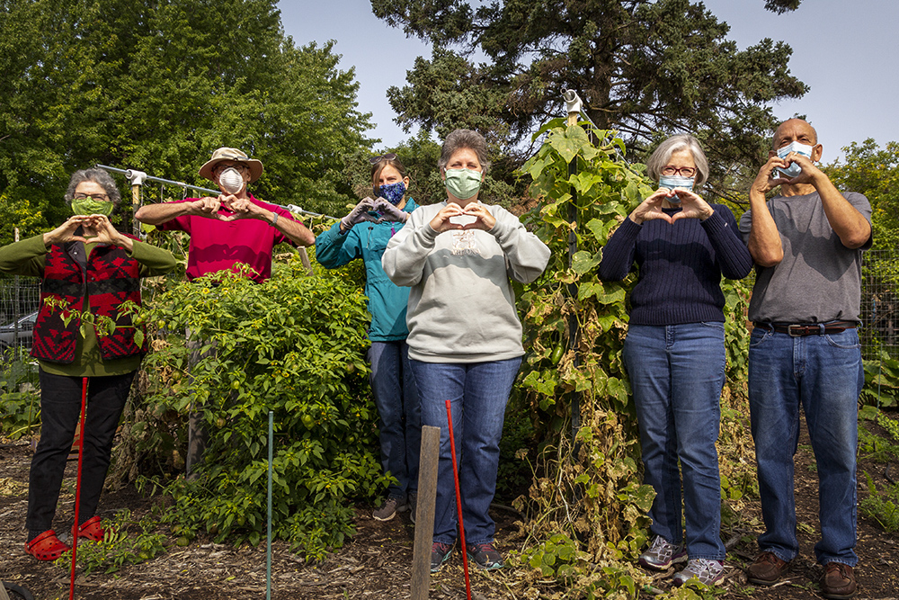 Group of 5 people standing in a green garden making a heart shape with their hands